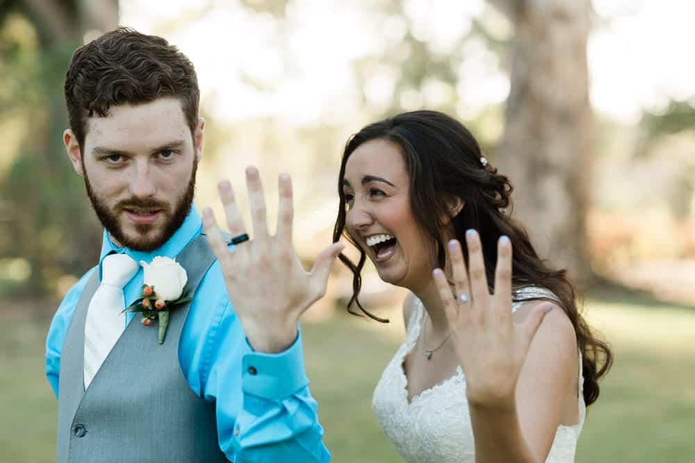 Bride laughs at groom as they show off their wedding rings. 